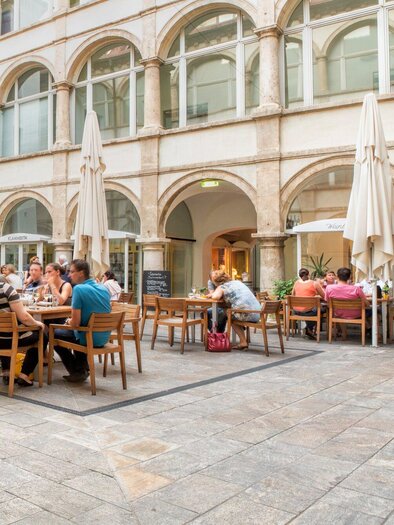 Ein gemütlicher Innenhof mit vielen Sitzplätzen. Gäste genießen das Essen unter Sonnenschirmen. | © Klapotetz