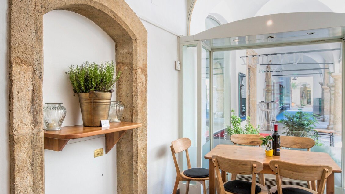 Ein einladendes Esszimmer mit Holzstühlen und einem Tisch. Im Hintergrund sind Pflanzen und ein heller Innenraum mit großen Fenstern sichtbar. | © Klapotetz