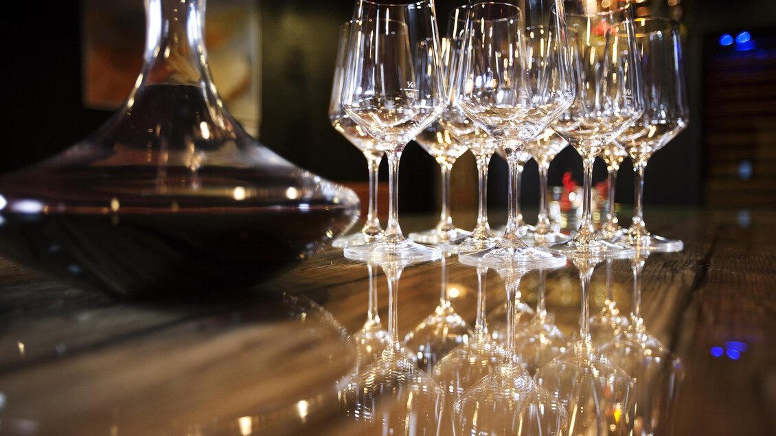 Eine stilvolle Weinausstellung mit einem Dekanter und einer Reihe von Gläsern. Die Gläser reflektieren das Licht auf einem eleganten Tisch. | © Rogner Bad Blumau