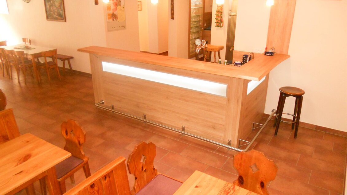 Eine gemütliche Innenansicht eines Restaurants mit einem Holzthekenbereich und rustikalen Tischen. Die Beleuchtung schafft eine einladende Atmosphäre. | © Lederer