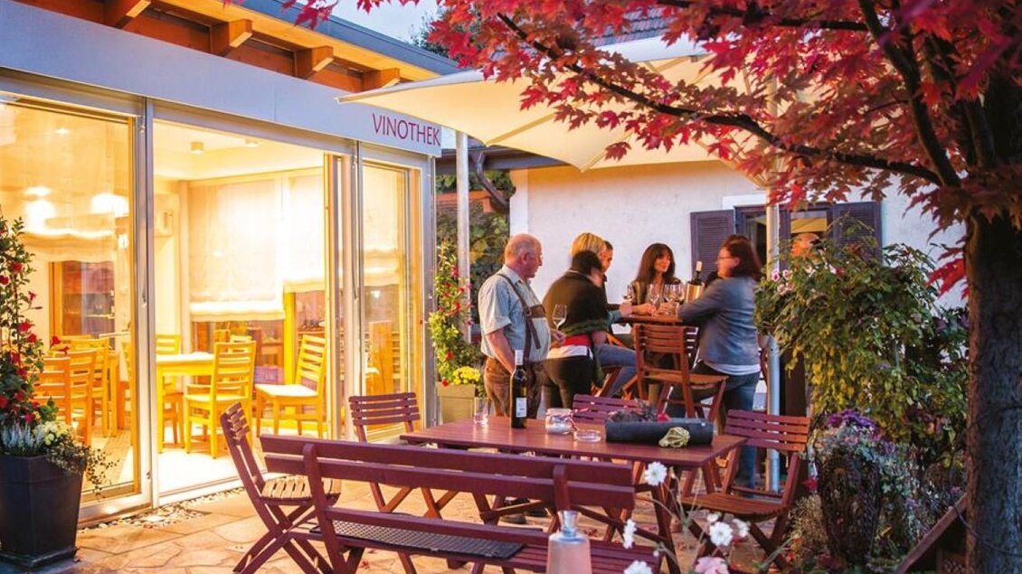 Eine gemütliche Terrasse mit einem Tisch und Stühlen, umgeben von bunten Herbstblättern. Menschen stehen zusammen und genießen die bereitgestellten Getränke. | © Grasmuck