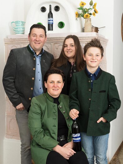 A family poses in traditional clothing in front of a fireplace. They are holding a bottle of wine and smiling at the camera. | © Weingut Klimbacher