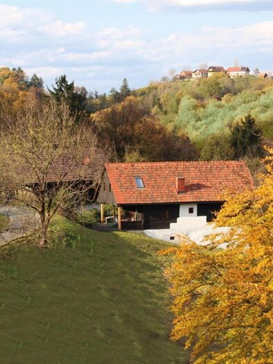 A rural scene with a small house and colorful autumn trees. Gentle hills are visible in the background. | © Pongratz