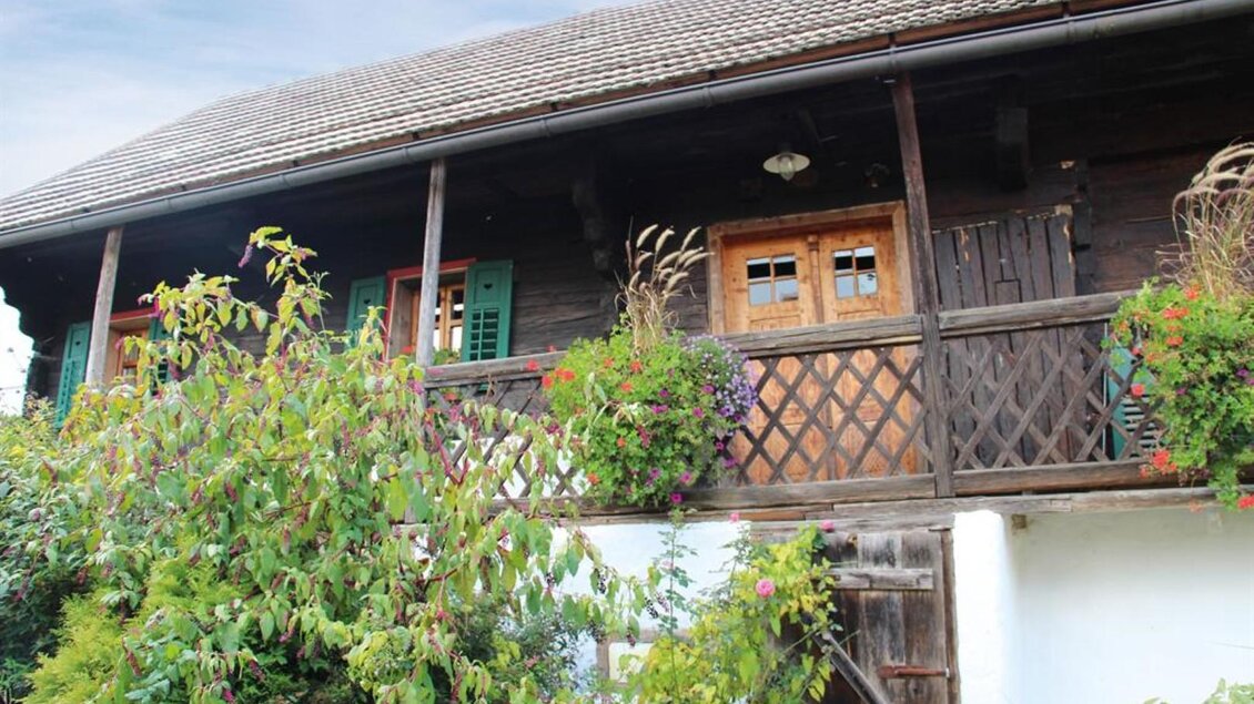 Ein traditionelles Holzhaus mit einem Balkon und bunten Blumenpflanzen. Die Wände sind teils grün bewachsen, was eine gemütliche Atmosphäre schafft. | © Pongratz