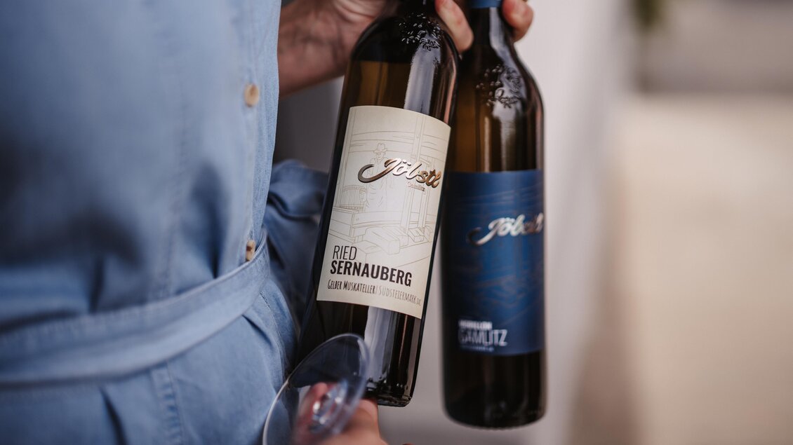 Zwei Weinflaschen werden von einer Person gehalten. Eine Flasche trägt das Etikett "Ried Sernauberg," während die andere eine dunklere Beschriftung hat. | © MichaelaLorber/WeingutJöbstl