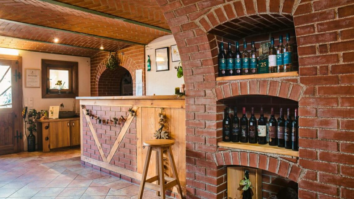 Ein gemütlicher Weinkeller mit Backsteinmauern und einer Holzbar. Regale mit Weinflaschen sind gut sichtbar und schaffen eine einladende Atmosphäre. | © Riegelnegg