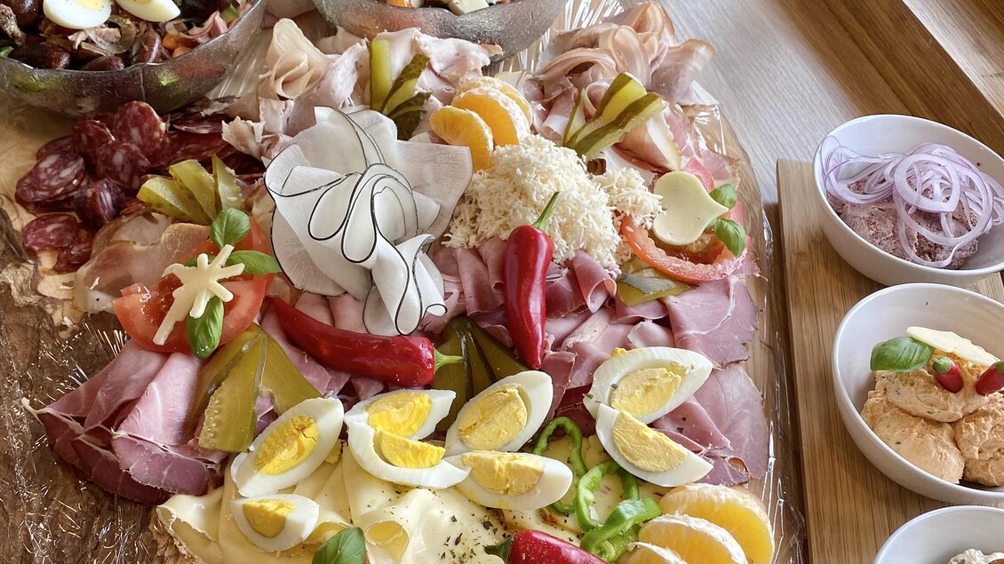 Eine bunte Auswahl an Aufschnitt, Käse und frischem Gemüse ist auf einem Tisch angerichtet. Verschiedene Schalen mit Salaten und Dips ergänzen das kulinarische Angebot.