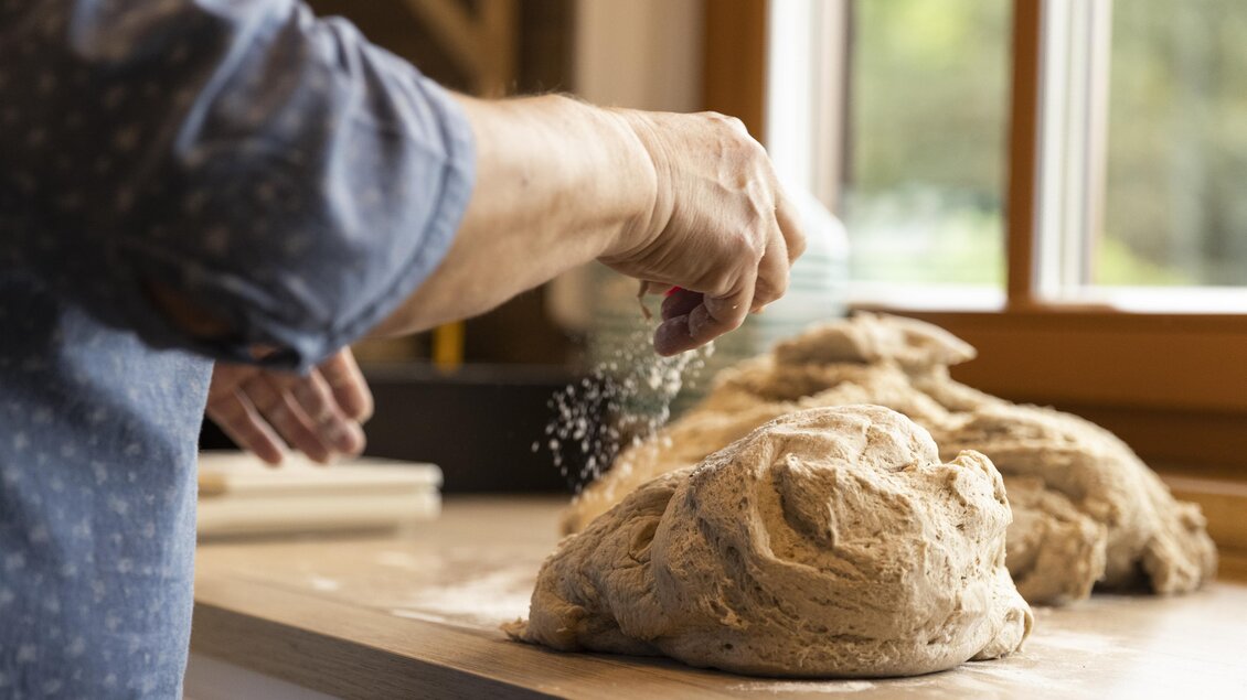 Eine Person streut Mehl über frischen Brotlaib. Im Hintergrund sind Fenster mit natürlichem Licht zu sehen. | © Lisa Resatz_Moonpower