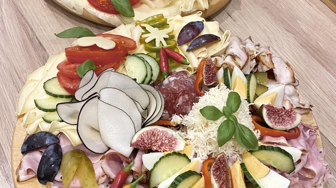 Eine ansprechende Platte mit verschiedenen Wurst- und Käsesorten, garniert mit frischen Früchten und Gemüse. Die Farben und Anordnung bieten einladende Visuals für einen Genussmoment.