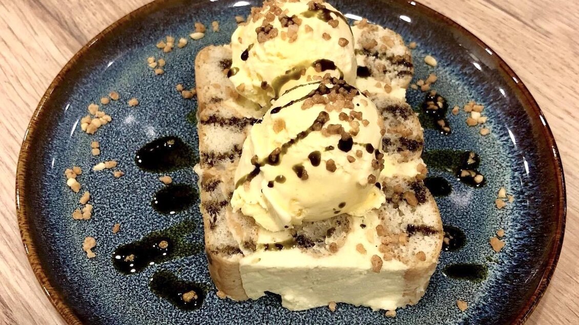 Ein köstlicher Dessertteller mit getoastetem Brot und zwei Kugeln Vanilleeis. Das Ganze ist mit Schokoladensauce und gehackten Nüssen garniert.