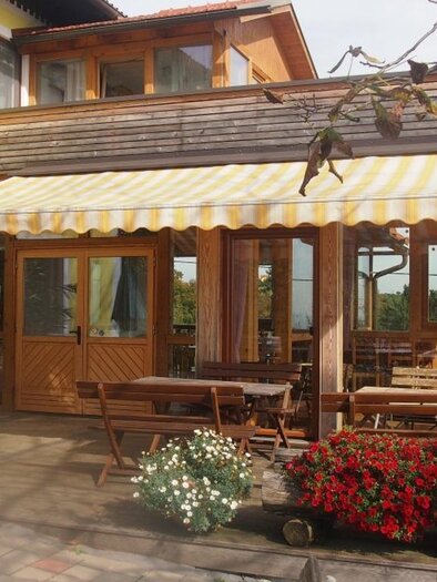 Eine gemütliche Terrasse mit einem Sonnenschirm und rustikalen Holzmöbeln. Bunte Blumen und Pflanzen verleihen dem Außenbereich einen einladenden Charme. | © Weingut Koller