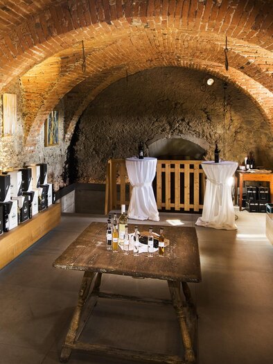 A wine cellar with a vaulted brick ceiling and wooden shelves. Bottles and glasses are set out on the table ready for a tasting. | © Weingut Malli