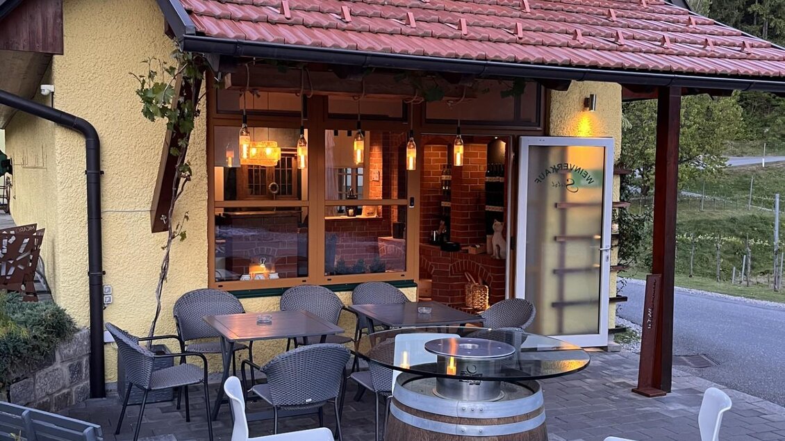 Eine Flasche Weißwein steht neben einem Weinglas auf einem Tisch. Im Hintergrund sind Bäume und eine Windmühle in einer sonnigen Landschaft zu sehen. | © Weingut Stelzl