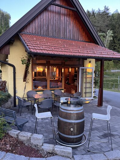 Eine Flasche Weißwein steht neben einem Weinglas auf einem Tisch. Im Hintergrund sind Bäume und eine Windmühle in einer sonnigen Landschaft zu sehen. | © Weingut Stelzl