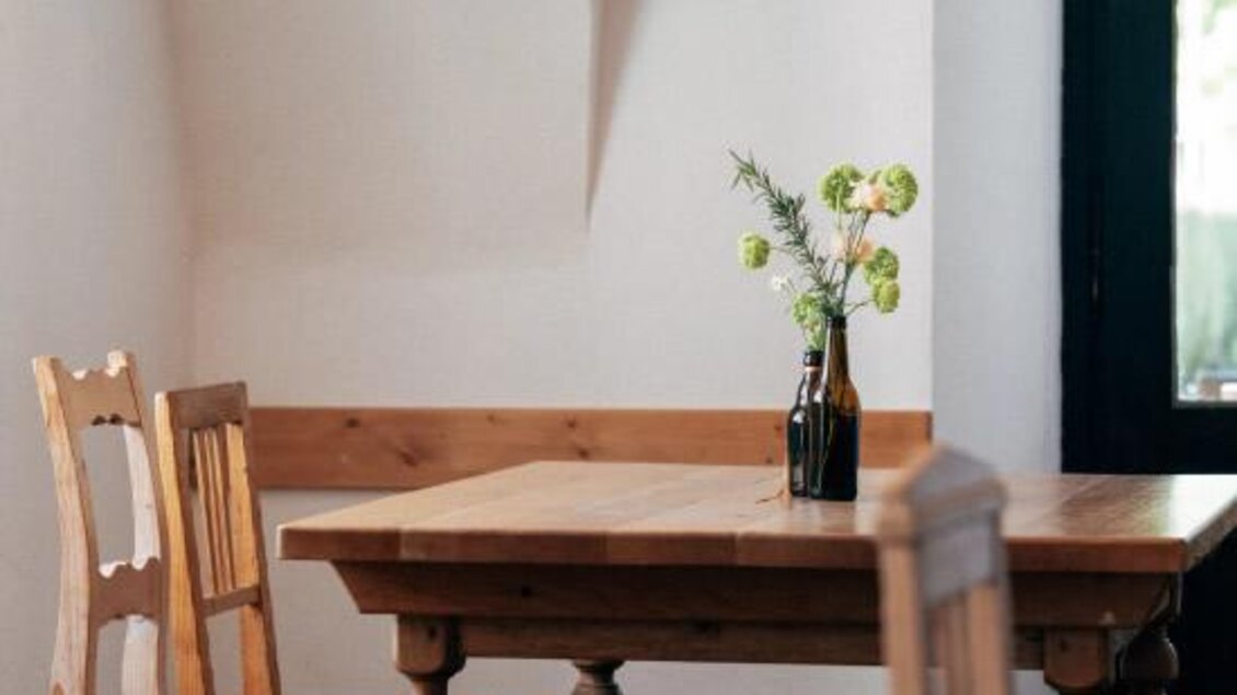 Ein gemütliches Restaurant mit einem Holztisch und Stühlen. Auf dem Tisch steht eine kleine Vase mit Blumen. | © Heldentheater