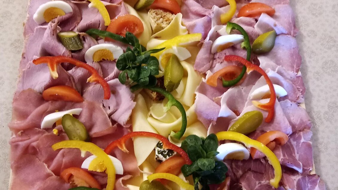 Eine große Auswahl an Wurst- und Käseplatten, hübsch dekoriert mit buntem Gemüse. Im Hintergrund sind einige Snacks und Beilagen sichtbar. | © Buschenschank Heschl