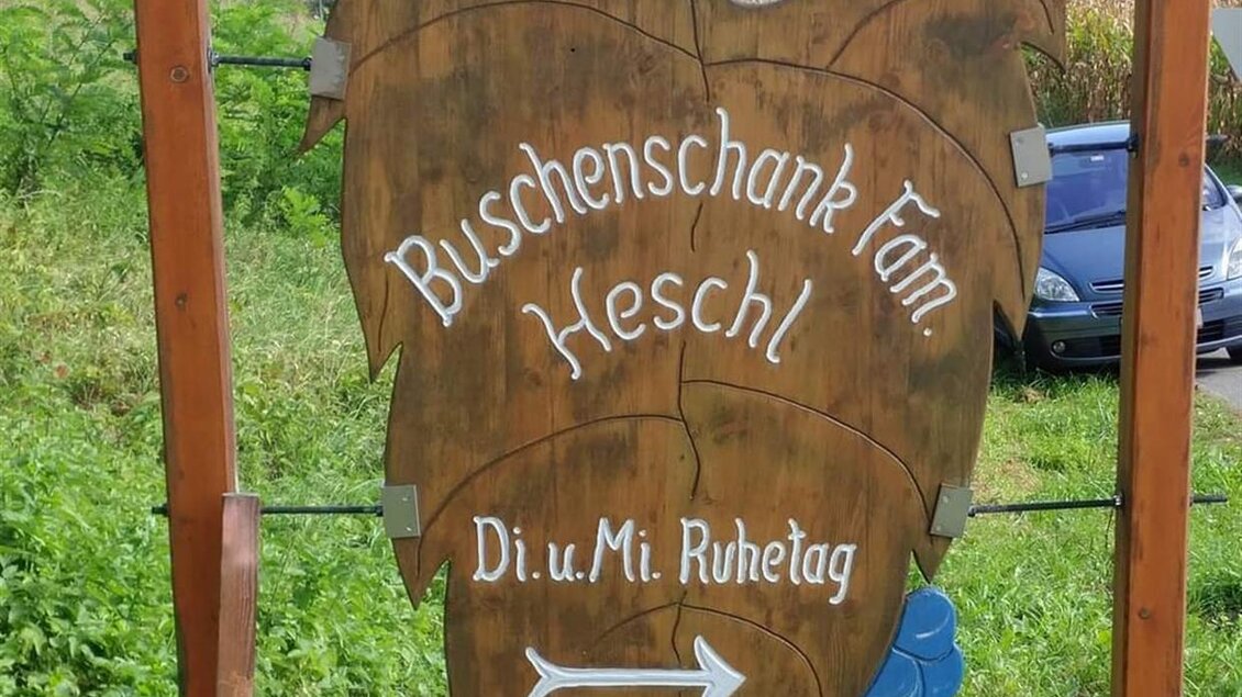Ein Holzschild eines Buschenschanks mit dem Namen "Meschl". Es zeigt Weintrauben und weist auf Öffnungszeiten hin. | © Buschenschank Heschl