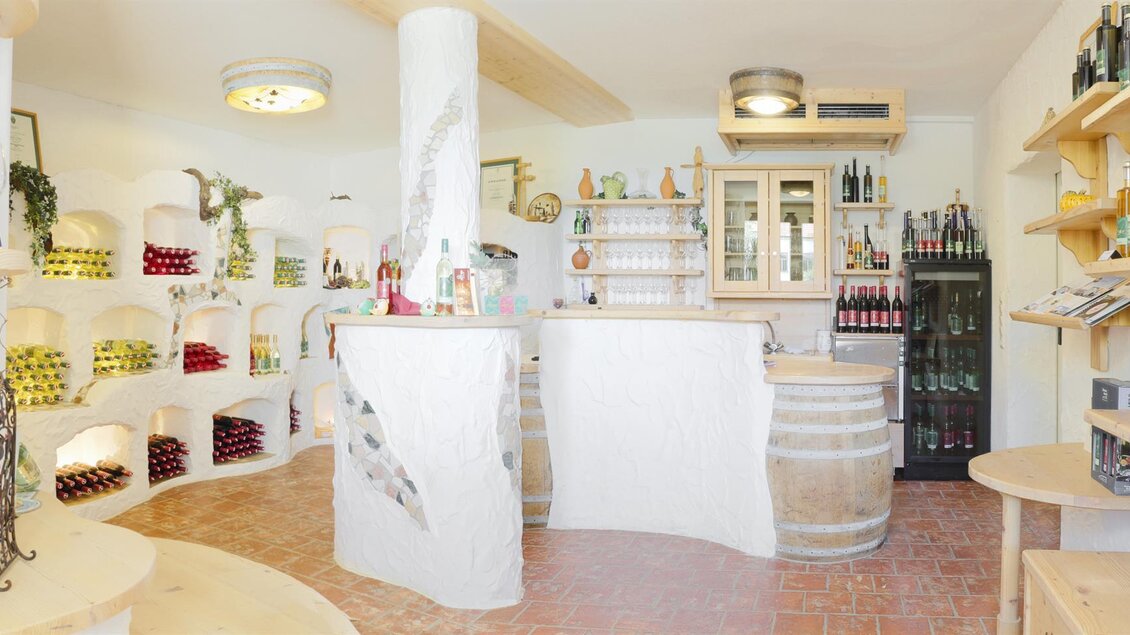 Ein einladender Verkostungsraum mit Holzregalen, die Flaschen präsentieren. Eine gemütliche Atmosphäre mit einem Empfangstresen und Weinfässern. | © Christoph Pohlner