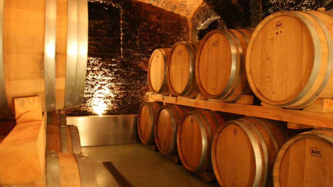 Ein Weinkeller mit Holzfässern auf Regalen. Die Wände sind aus Stein und die Beleuchtung ist gedämpft. | © Lederer