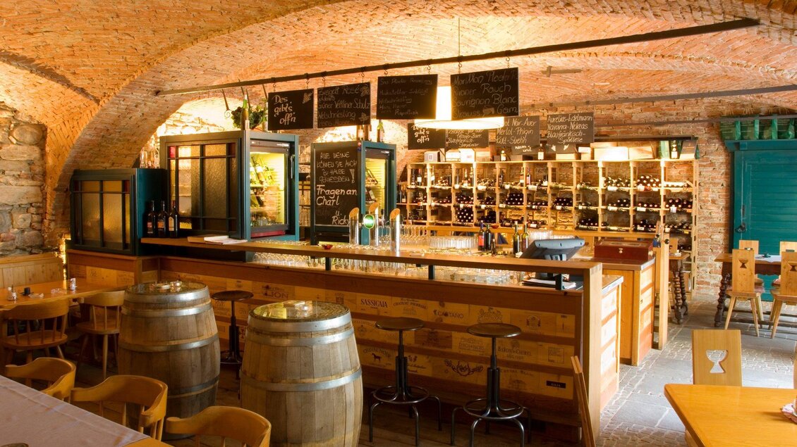 Eine gemütliche Weinbar mit einem langen Bartresen und Regalen voller Weine. Die Wände sind aus Ziegelstein, was eine warme Atmosphäre schafft. | © Klarmann