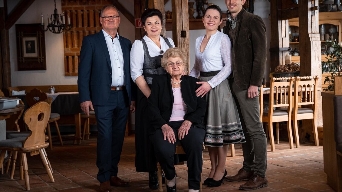 Eine Gruppe von fünf Personen steht in einem rustikalen Restaurant. Eine ältere Frau sitzt in der Mitte, umgeben von drei jüngeren Personen und einem Mann. | © Weinrefugium Brolli