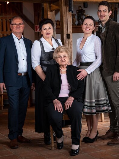 A group of five people is standing in a rustic restaurant. An older woman is sitting in the middle, surrounded by three younger people and a man. | © Weinrefugium Brolli