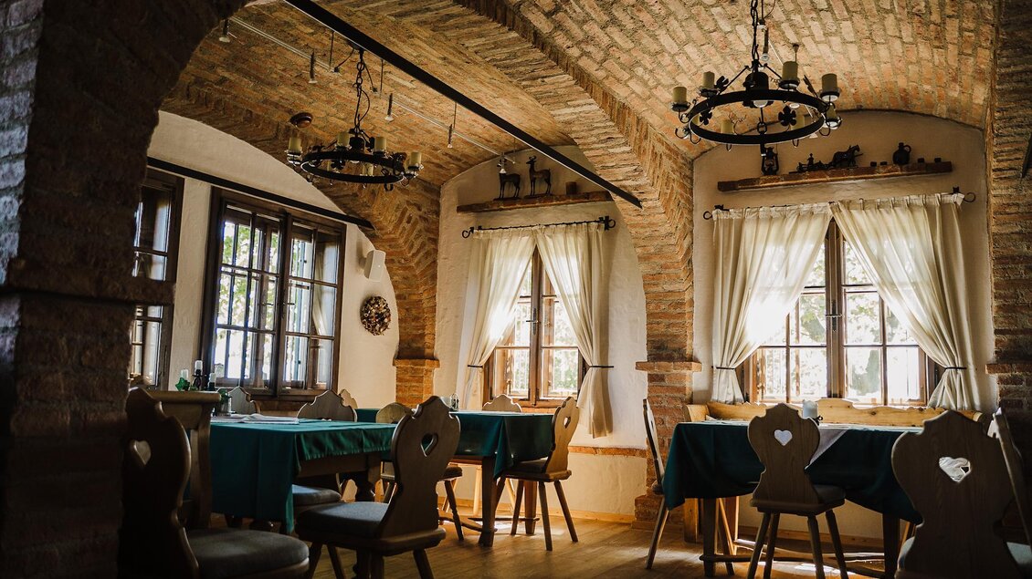 Ein gemütlicher Speisesaal mit Holztischen und Stühlen. Große Fenster lassen viel Licht herein und der rustikale Steinbogen verleiht einen einladenden Charakter. | © Weinrefugium Brolli