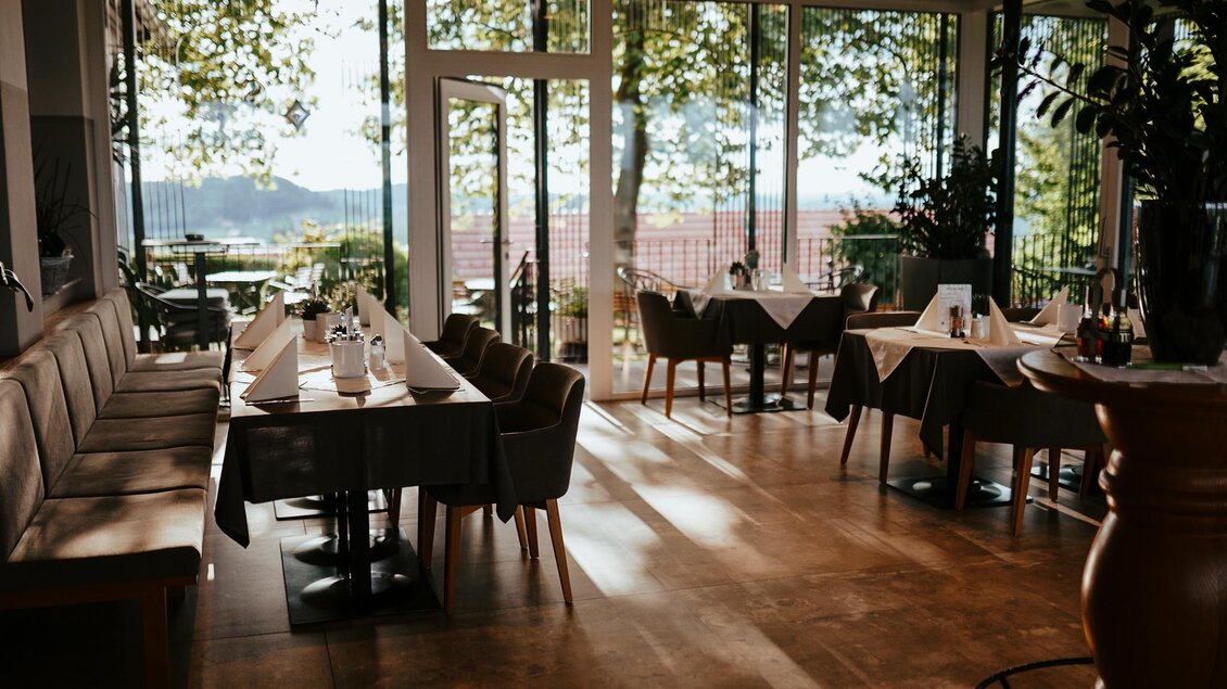 Ein modernes Restaurant mit einem gemütlichen Innenraum und großen Fenstern. Die Tische sind elegant gedeckt und bieten einen Blick ins Grüne. | © Weinrefugium Brolli