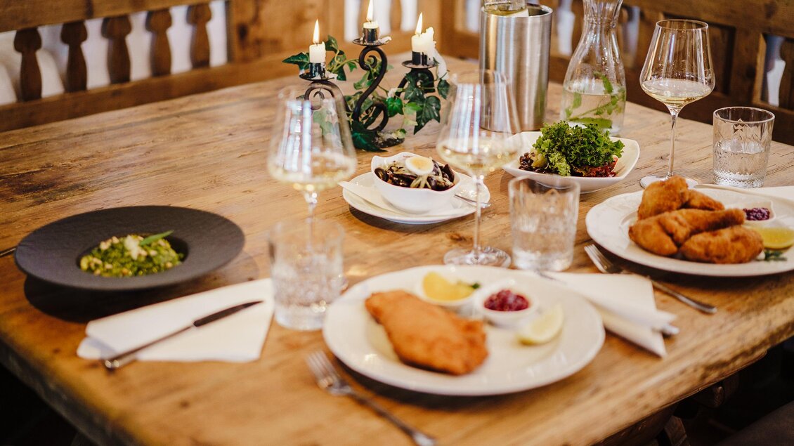 Ein einladender Tisch mit verschiedenen köstlichen Gerichten, darunter Fisch und Salat. Die Atmosphäre wird durch Kerzen und Weingläser ergänzt. | © Weinrefugium Brolli