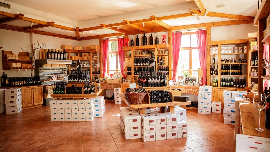 Ein gemütlicher Weinausschankraum mit Regalen voller Weinflaschen. Helle Fenster und Holzmöbel verleihen dem Raum eine einladende Atmosphäre.