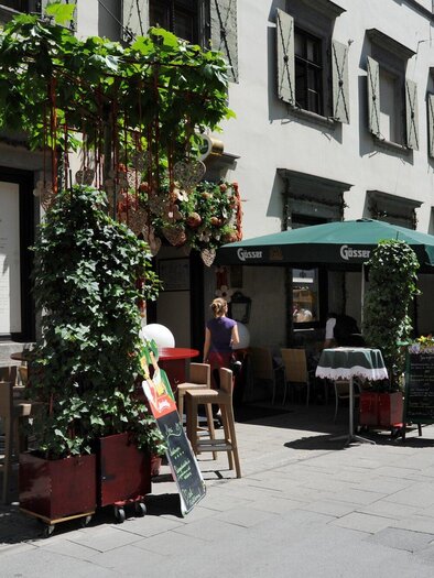 A charming street with cozy terraces and green plants. The buildings are designed in a traditional style and invite you to linger. | © Welscher Stub'n