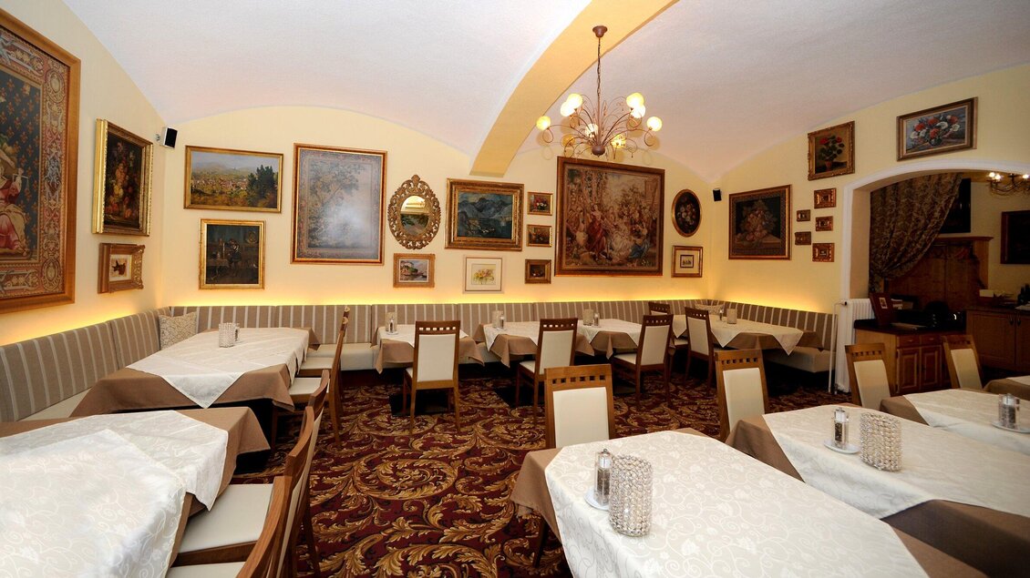 Ein elegantes Restaurant mit Tischen, die mit weißen Tischtüchern gedeckt sind. Die Wände sind mit verschiedenen Kunstwerken dekoriert und die Beleuchtung schafft eine gemütliche Atmosphäre. | © Welscher Stub'n