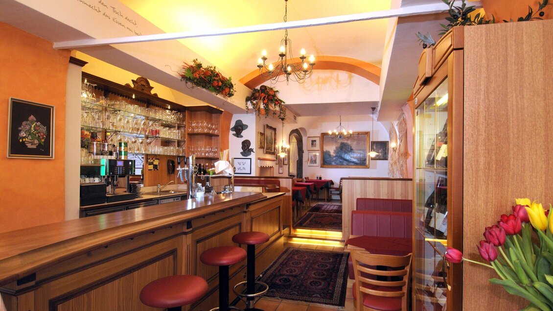 Eine gemütliche Bar mit einem Holztheken und roten Barhockern. Im Hintergrund sind Tische und eine einladende Atmosphäre zu sehen. | © Welscher Stub'n