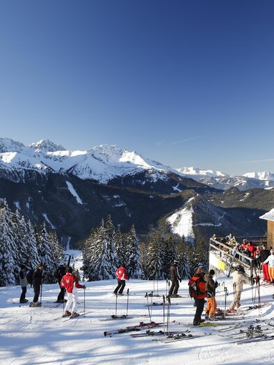 A picturesque ski landscape with snow-covered mountains and trees. Skiing individuals are enjoying the clear sky and the sun. | © Herbert Raffalt