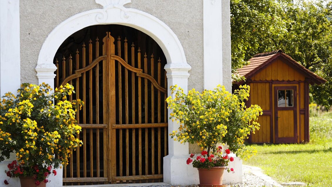 Ein schöner Eingang mit einer Holzpforte und blühenden Pflanzen. Im Hintergrund steht ein kleines Holzhaus. | © Bernhard Bergmann