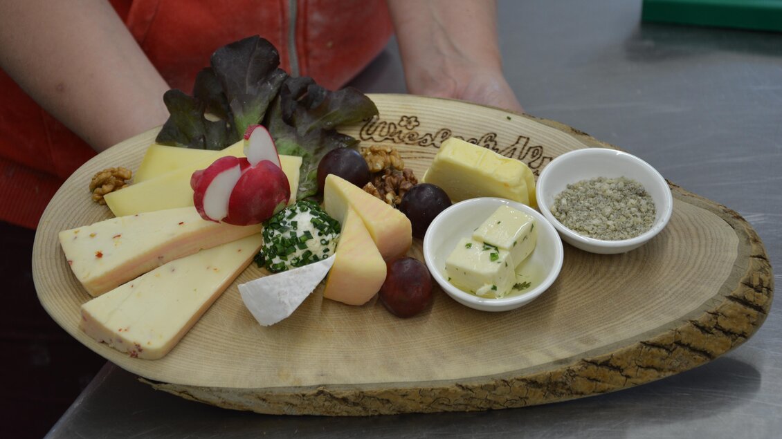 Ein rustikales Käsebrett mit verschiedenen Käsesorten, Trauben und Radieschen. Dazu gibt es frische Kräuter und Butter in kleinen Schalen. | © eigen
