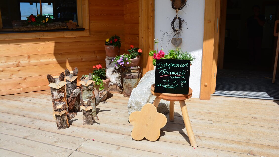 Ein einladender Eingang mit einer Holzveranda und blühenden Blumen. Eine Tafel mit einem Menü steht neben Holzscheiten. | © eigen