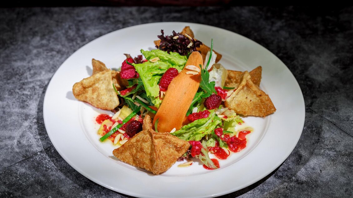 Ein bunter Salat mit frischem Gemüse und Himbeeren, garniert mit knusprigen Teigtaschen. Der Salat wird auf einem weißen Teller serviert. | © martin huber