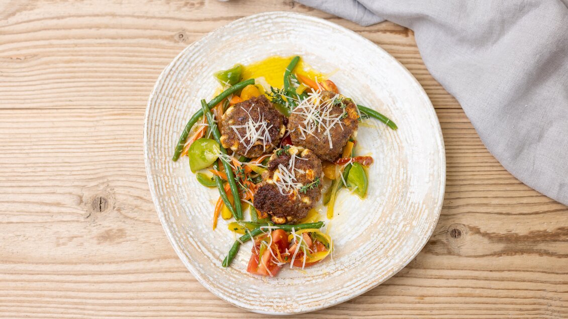 Ein köstliches Gericht mit frittierten Fleischbällchen, serviert auf einem Bett aus buntem Gemüse. Das Essen ist mit frischem Käse und einer hellen Soße verfeinert. | © ©Martin Huber