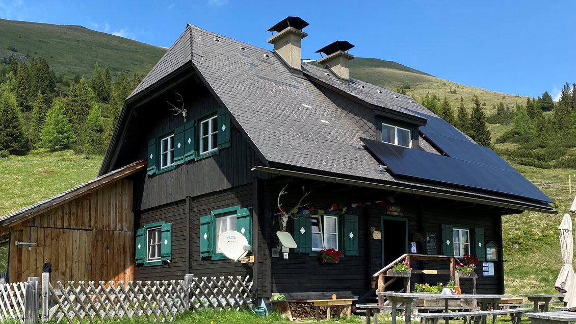 Ein gemütliches schwarzes Haus in der Natur mit grünen Fensterläden. Umgeben von Wiesen und Bergen unter einem blauen Himmel. | © Erlebnisregion Murtal