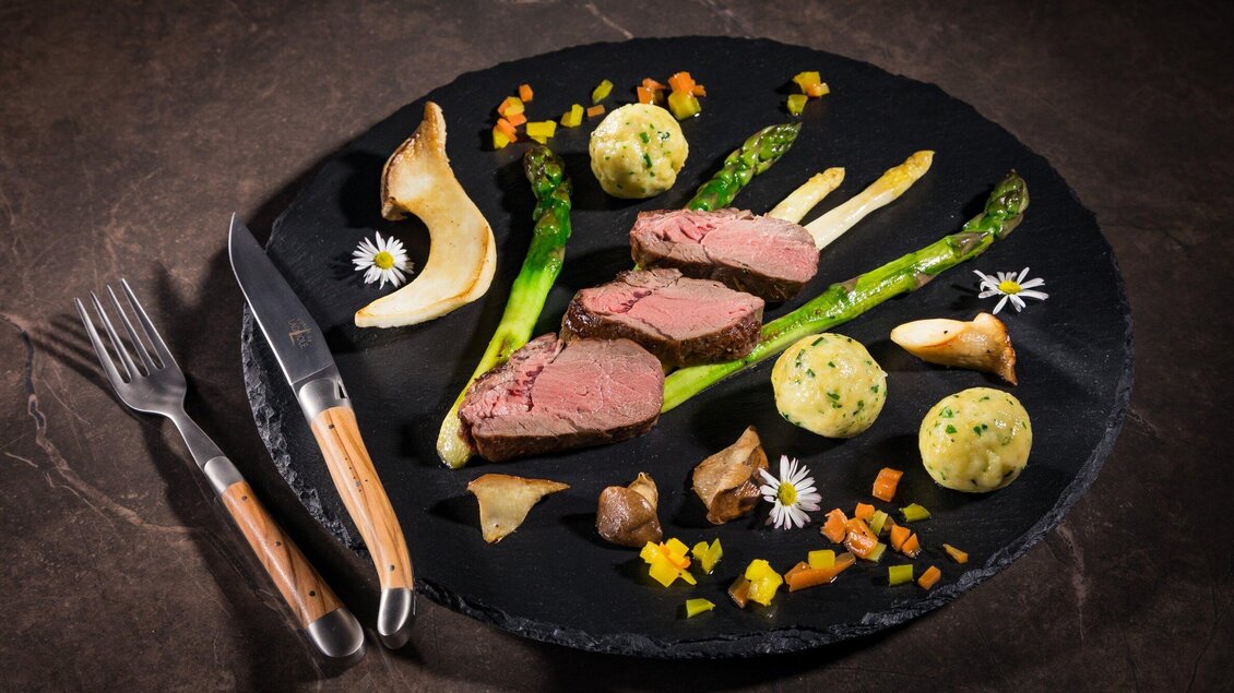 Ein elegantes Gericht mit zartem Fleisch, grünem Spargel und buntem Gemüse. Der Teller ist stilvoll angerichtet und bietet eine ansprechende Präsentation. | © J-Werner Krug