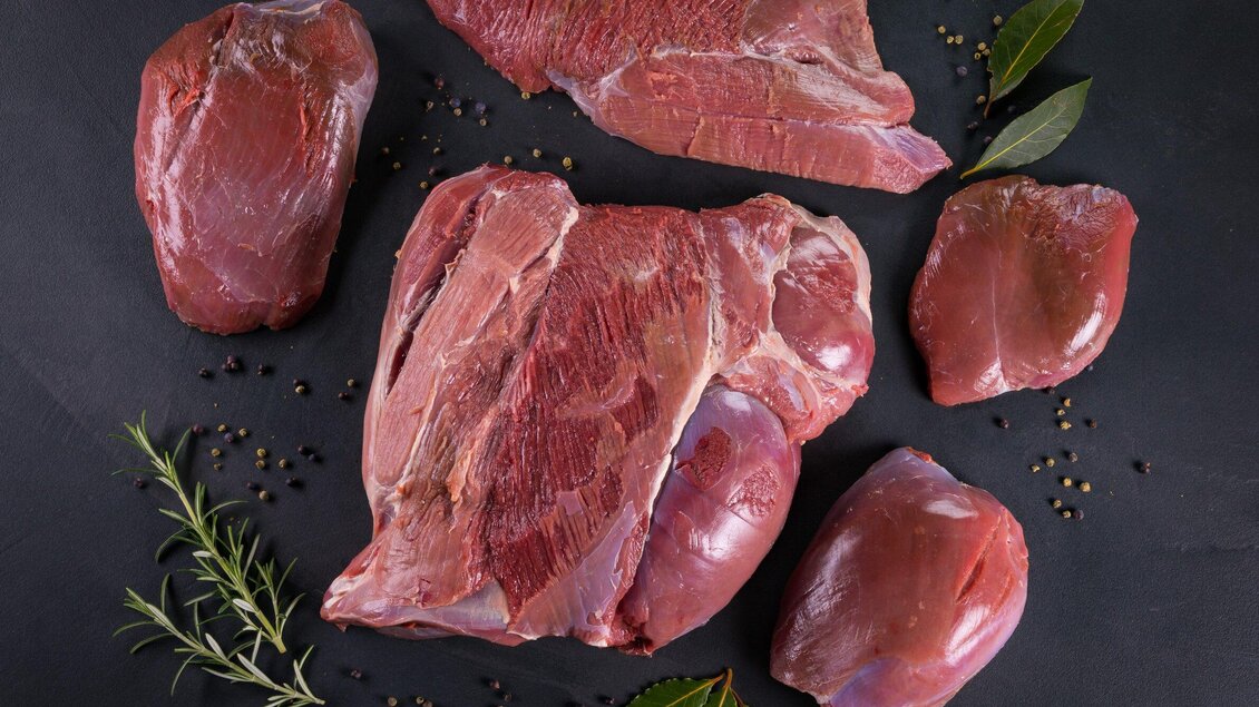 Frisches rotes Fleisch auf einem dunklen Hintergrund, umgeben von Kräutern wie Rosmarin und Lorbeerblättern. Ideal für eine ansprechende Präsentation in der Küche. | © J-Werner Krug