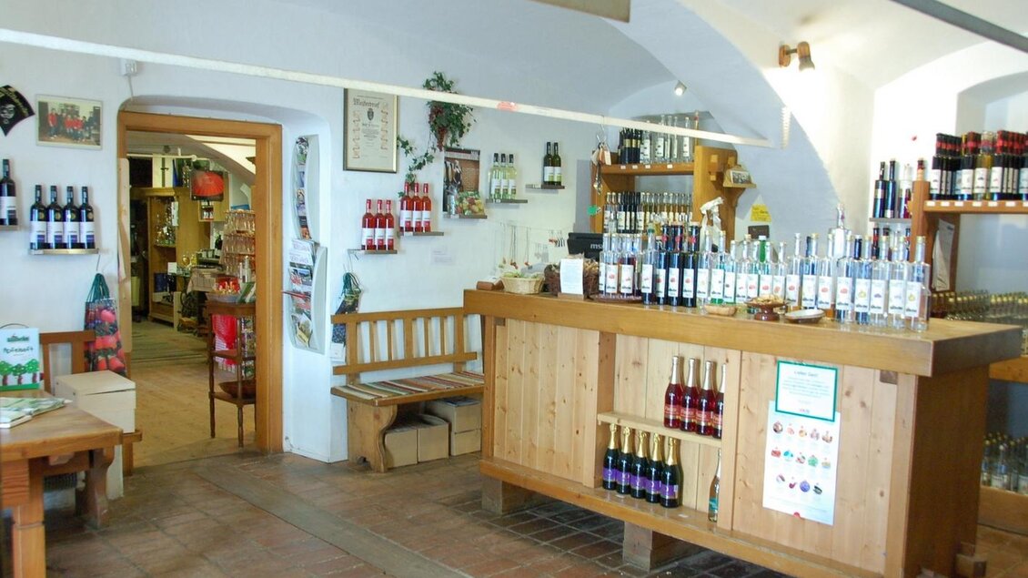 Ein einladendes Geschäft mit Holzregalen, die verschiedene Flaschen mit Getränken zeigen. Im Hintergrund sind Tische und weitere Regale zu sehen. | © Wilhelm Spezialitäten
