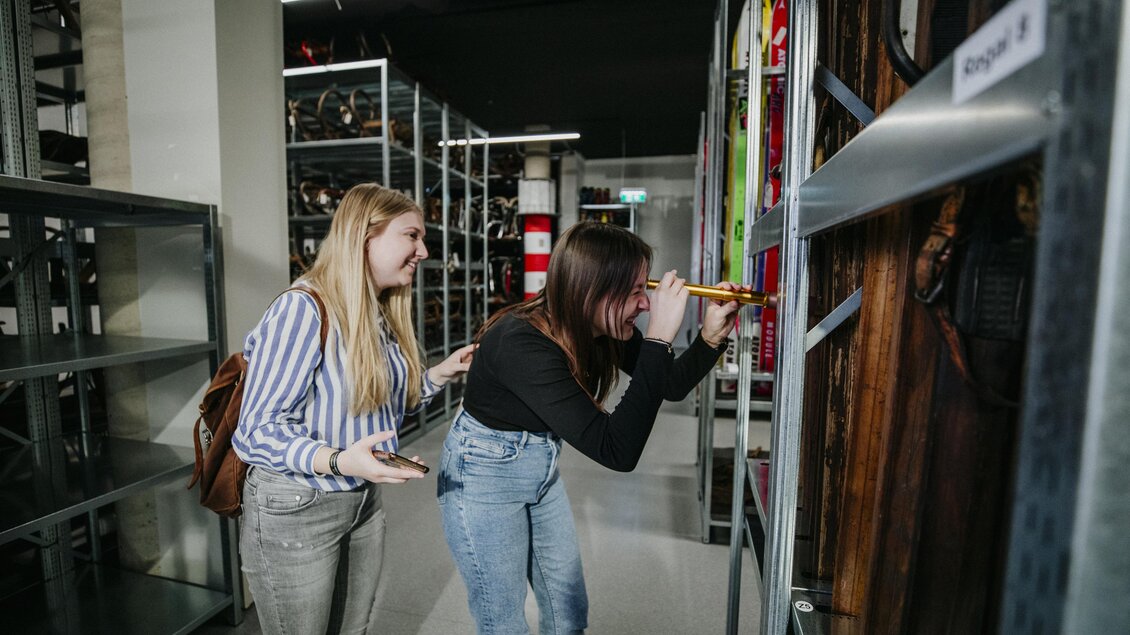 Zwei Frauen schauen neugierig in ein Regal voller Objekte. Sie scheinen an den Exponaten interessiert zu sein und haben viel Spaß dabei. | © nicoleseiser.at
