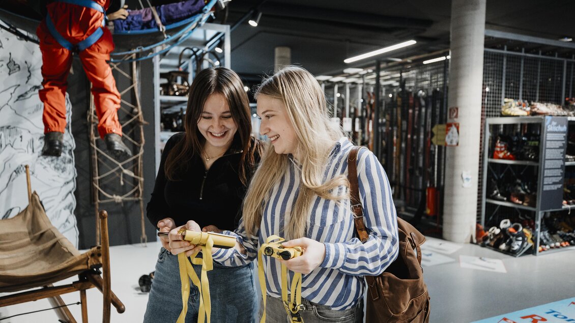 Zwei Frauen stehen in einem Kletterzentrum und halten Sicherheitsgurte. Sie lächeln und scheinen sich auf die bevorstehende Aktivität zu freuen. | © nicoleseiser.at