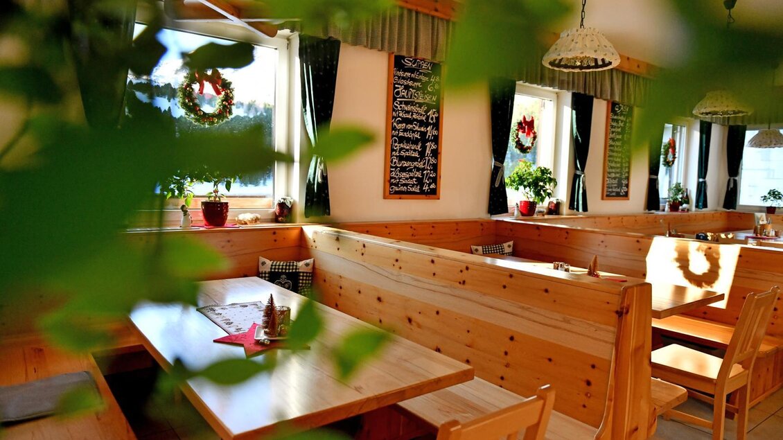 Ein gemütliches Restaurant mit Holzmöbeln und Pflanzen. An den Wänden hängen dekorative Elemente und eine Tafel mit Menüangeboten. | © Andreas Wieser