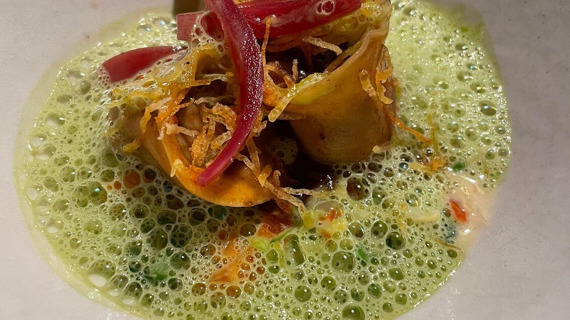 Ein kunstvolles Gericht mit einer grünen Schaumsoße, darauf befinden sich gedämpfte Artischocken und rote Zwiebelstreifen. Das Arrangement ist ansprechend und modern. | © Andreas Wieser