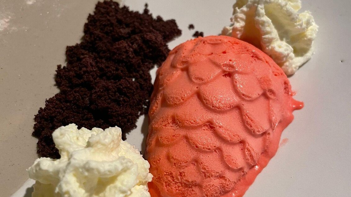 Ein Dessertteller mit einer Erdbeere aus Eis, umgeben von Schlagsahne und Schokoladenkrümeln. Die Farben sind lebendig und ansprechend. | © Andreas Wieser
