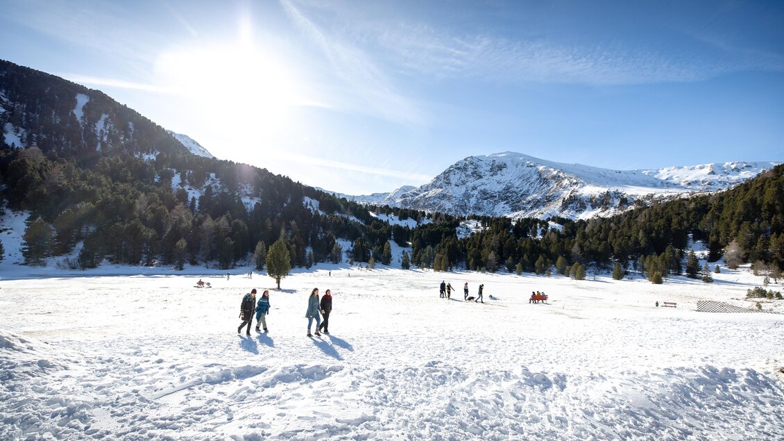 Eine verschneite Landschaft mit Menschen, die auf dem Schnee spazieren. Im Hintergrund sind Berge und ein klarer blauer Himmel zu sehen. | © Tom Lamm
