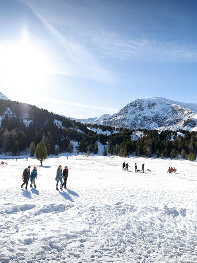 A snowy landscape with people walking on the snow. In the background, there are mountains and a clear blue sky. | © Tom Lamm